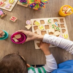 Menor realizando una actividad de aprendizaje con letras y juguetes educativos junto a una profesional de atención temprana.