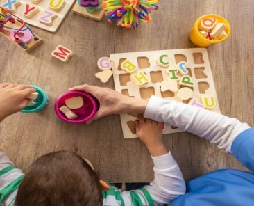 Menor realizando una actividad de aprendizaje con letras y juguetes educativos junto a una profesional de atención temprana.