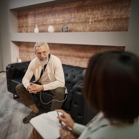 Hombre en sesión de terapia psicológica hablando con una profesional que toma notas en una consulta moderna