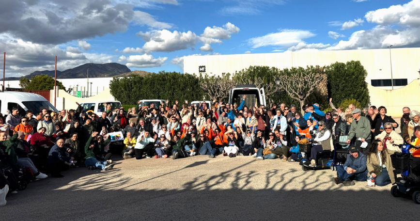 Grupo numeroso de personas participantes en el encuentro de asociaciones de COCEMFE Alicante en Novelda, posando al aire libre en una jornada inclusiva.