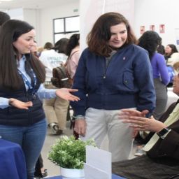 Participantes conversan en un estand de la IV Feria de Empleo de COCEMFE Sevilla con una mujer usuaria de silla de ruedas.