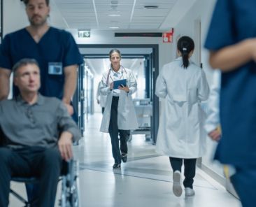 Paciente en silla de ruedas acompañado por profesionales sanitarios en un hospital, imagen que representa la atención sanitaria inclusiva y centrada en las personas.