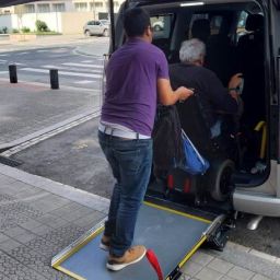 Persona en silla de ruedas accediendo a un taxi adaptado mediante rampa con ayuda en una calle urbana