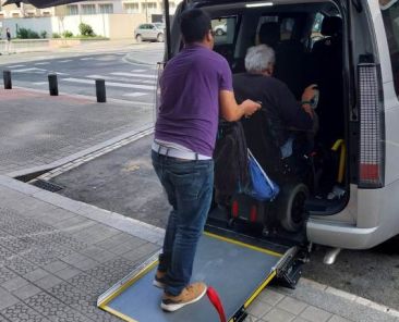 Acceso a taxi adaptado en entorno urbano Persona en silla de ruedas accediendo a un taxi adaptado mediante rampa con ayuda en una calle urbana