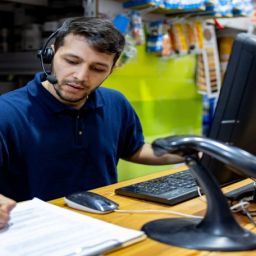 Trabajador atendiendo tareas de gestión y atención al cliente en el mostrador de una tienda.