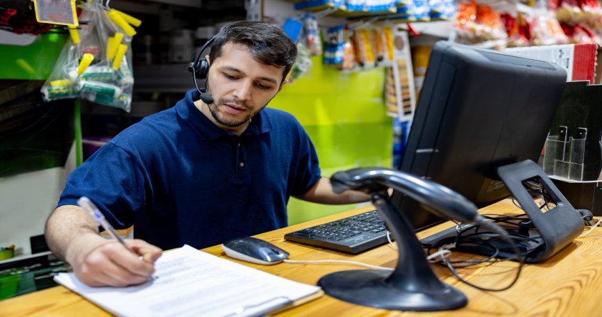 Trabajador atendiendo tareas de gestión y atención al cliente en el mostrador de una tienda.