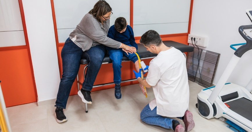 Profesional sanitario atiende a un niño en sesión de atención temprana con acompañamiento familiar