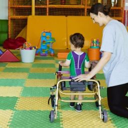 Profesional apoya a un niño con discapacidad en ejercicios de Atención Temprana con andador en sala adaptada