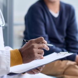 Profesional sanitario conversa con una persona durante una consulta médica mientras toma notas en un portapapeles