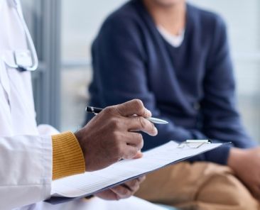 Profesional sanitario conversa con una persona durante una consulta médica mientras toma notas en un portapapeles