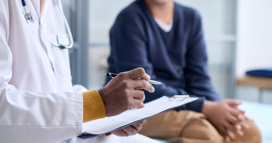 Profesional sanitario conversa con una persona durante una consulta médica mientras toma notas en un portapapeles