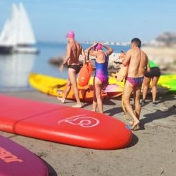 Personas preparándose para deporte adaptado con tablas y kayaks en la playa