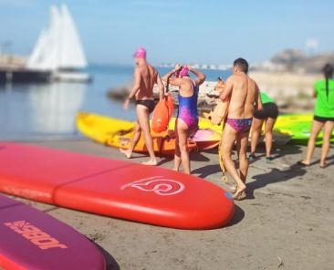 Personas preparándose para deporte adaptado con tablas y kayaks en la playa