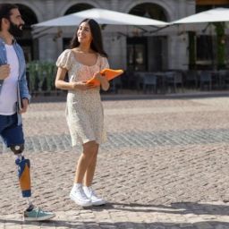 Persona con prótesis camina por la ciudad con naturalidad Persona con prótesis en la pierna paseando por una plaza junto a otra persona en un entorno urbano accesible