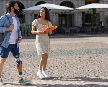 Persona con prótesis camina por la ciudad con naturalidad Persona con prótesis en la pierna paseando por una plaza junto a otra persona en un entorno urbano accesible