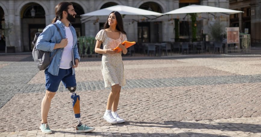 Persona con prótesis en la pierna paseando por una plaza junto a otra persona en un entorno urbano accesible