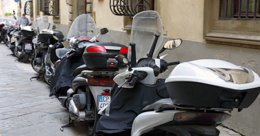 Varias motocicletas estacionadas en una acera, ocupando parte del espacio peatonal en una calle urbana.