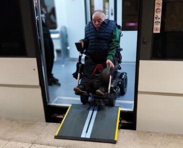Persona usuaria de silla de ruedas eléctrica accede a un tren de Renfe Cercanías mediante una rampa portátil.