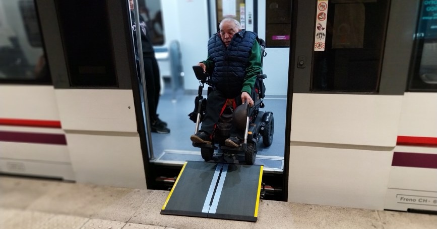 Persona usuaria de silla de ruedas eléctrica accede a un tren de Renfe Cercanías mediante una rampa portátil.