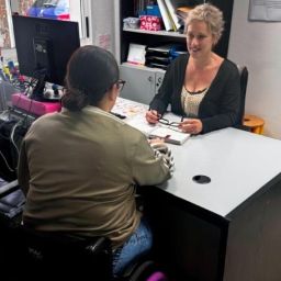 Profesional de COGAMI atiende a una mujer usuaria de silla de ruedas durante una sesión de orientación y acompañamiento individual.