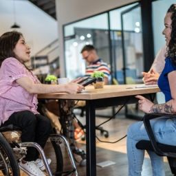 Inclusión laboral de las personas con acondroplasia Mujer con acondroplasia, usuaria de silla de ruedas, participa en una reunión de trabajo en una oficina accesible.