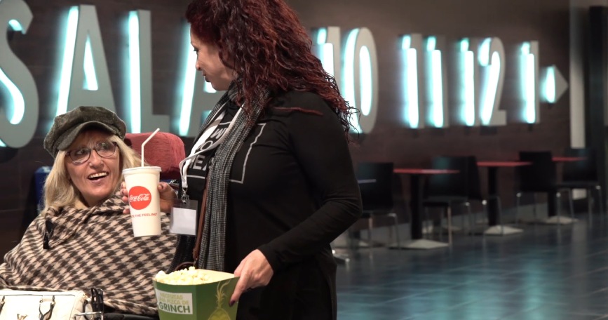 Mujer con discapacidad acompañada por una profesional de apoyo durante una actividad de ocio en un cine, promoviendo la autonomía personal y la inclusión social.