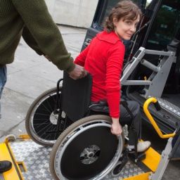 Persona usuaria de silla de ruedas accediendo a un vehículo adaptado mediante una plataforma elevadora con apoyo de otra persona.