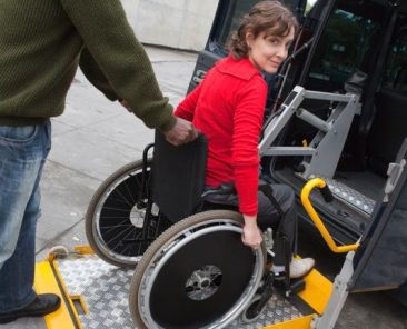 Acceso a un vehículo de transporte adaptado Persona usuaria de silla de ruedas accediendo a un vehículo adaptado mediante una plataforma elevadora con apoyo de otra persona.