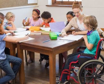 Educación inclusiva en el aula Docente y grupo de escolares, entre ellos un alumno usuario de silla de ruedas, participan juntos en una actividad en un aula inclusiva.