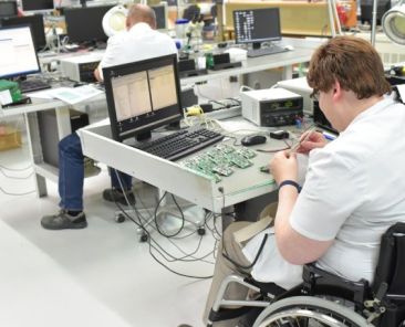 Persona con discapacidad en un entorno laboral inclusivo Persona usuaria de silla de ruedas trabaja en un laboratorio de electrónica como ejemplo de inclusión laboral de personas con discapacidad.