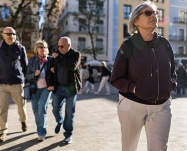 Mujer mayor caminando por una plaza urbana mientras otras personas pasean, representando la jubilación anticipada de las personas con discapacidad.