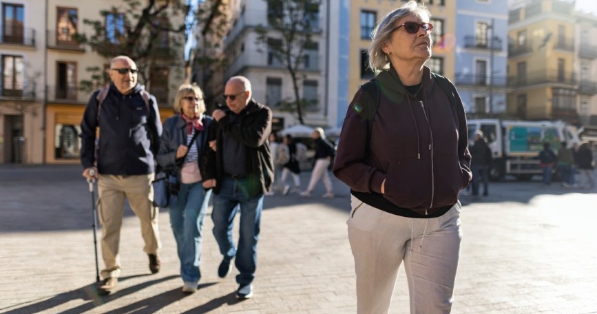 Mujer mayor caminando por una plaza urbana mientras otras personas pasean, representando la jubilación anticipada de las personas con discapacidad.