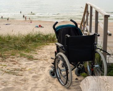 Accesibilidad en las playas para garantizar el acceso al mar Silla de ruedas junto a una pasarela de acceso a una playa con el mar al fondo, representando la necesidad de mejorar la accesibilidad del litoral.
