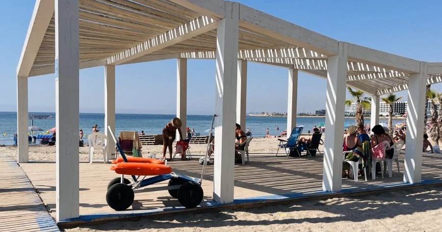 Punto accesible de una playa de Alicante con pérgola, pasarela y silla anfibia para facilitar el acceso al baño de personas con discapacidad.