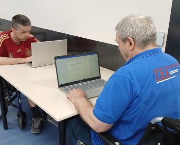 Dos personas usuarias de silla de ruedas utilizan ordenadores portátiles en las instalaciones de AGORA.