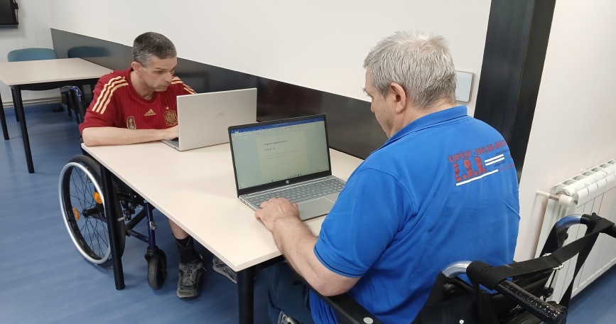 Dos personas usuarias de silla de ruedas utilizan ordenadores portátiles en las instalaciones de AGORA.
