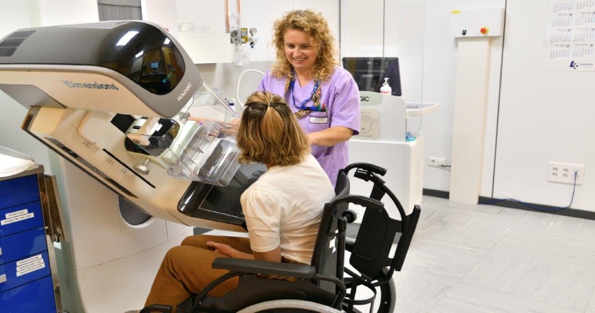 Mujer usuaria de silla de ruedas realizándose una mamografía con apoyo de una profesional sanitaria.