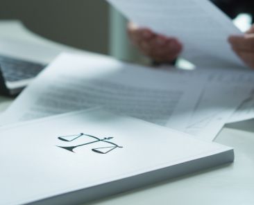 ADEE y cumplimiento de la normativa frente a espectáculos denigrantes Carpeta con el símbolo de la justicia sobre una mesa con documentos, mientras una persona revisa papeles.