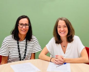 Dos representantes de COCEMFE Alicante y Benigar sentadas ante los documentos del convenio de colaboración para favorecer el empleo de personas con discapacidad.