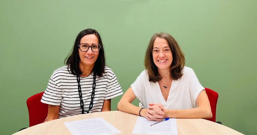Dos representantes de COCEMFE Alicante y Benigar sentadas ante los documentos del convenio de colaboración para favorecer el empleo de personas con discapacidad.