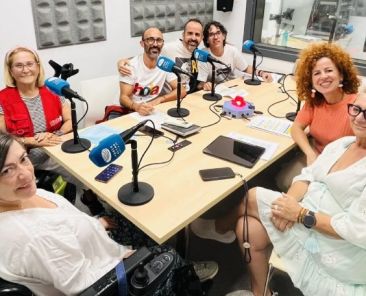 Ocho personas, entre ellas una mujer usuaria de silla de ruedas, reunidas alrededor de una mesa con micrófonos en el estudio de Radio Altea.