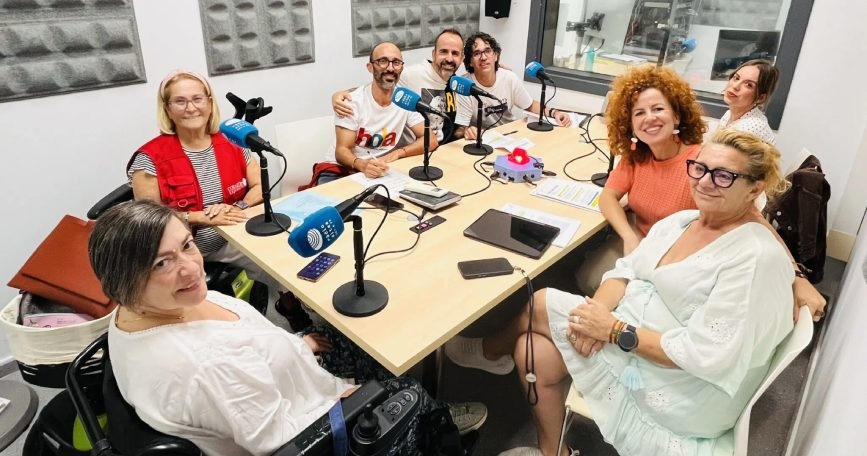 Ocho personas, entre ellas una mujer usuaria de silla de ruedas, reunidas alrededor de una mesa con micrófonos en el estudio de Radio Altea.
