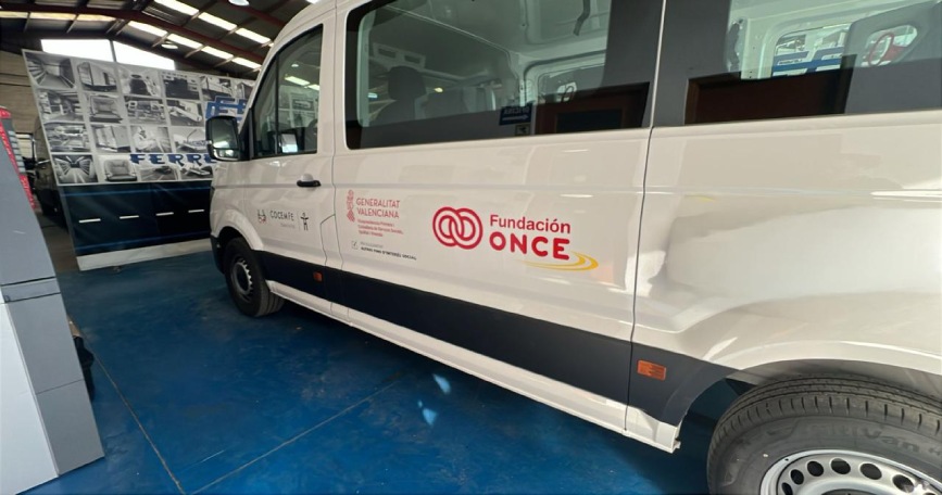Furgoneta blanca de transporte adaptado de COCEMFE Castelló, con los logotipos de Fundación ONCE y Generalitat Valenciana, estacionada en una nave.
