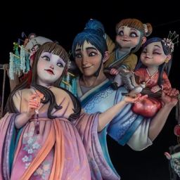 Monumento fallero iluminado de noche con figuras de estética oriental, personajes infantiles y un gato naranja en las Fallas de Valencia.