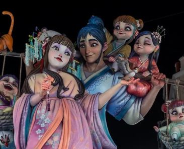 COCEMFE CV propone nueve medidas para unas Fallas accesibles Monumento fallero iluminado de noche con figuras de estética oriental, personajes infantiles y un gato naranja en las Fallas de Valencia.