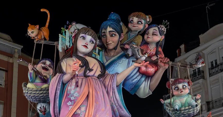 Monumento fallero iluminado de noche con figuras de estética oriental, personajes infantiles y un gato naranja en las Fallas de Valencia.