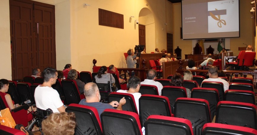 Personas asistentes a una jornada de COCEMFE Sevilla en Écija observan una presentación titulada «El prejuicio. La barrera invisible».