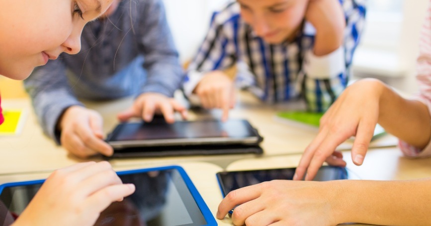 Varios niños y niñas utilizan tabletas digitales alrededor de una mesa durante una actividad educativa.