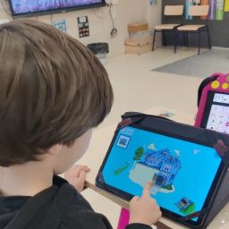 Recursos tecnológicos para una educación inclusiva Alumno utilizando una tableta educativa junto a un dispositivo de comunicación con pictogramas en un aula.