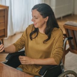 Mujer usuaria de silla de ruedas utiliza un teléfono móvil en su domicilio.